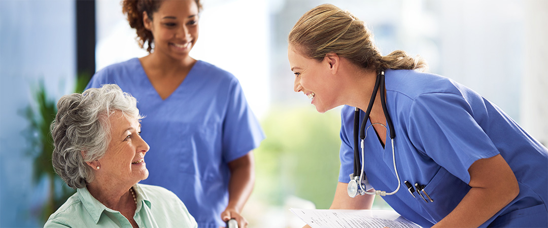 two nurses in blue scrubs with an elderly lady in a wheelchair