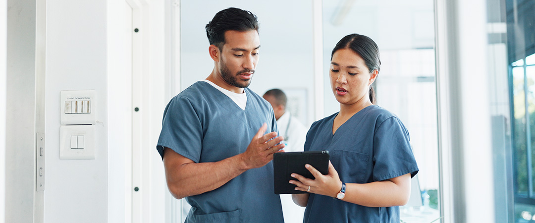 two nurses talking to each other in the hallway. Both wearing scrubs