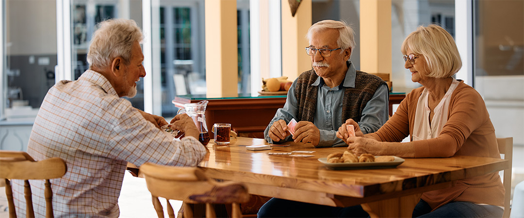Group of friends sitting at a table playing cards and eating pastries while chatting.