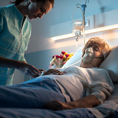 Nurse checking on a woman wearing an oxygen mask while in a hospital bed.